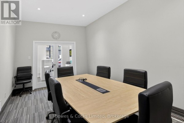 Boardroom with a large light wood table, six black chairs, and glass double doors. - 269 Charlotte Street, Peterborough