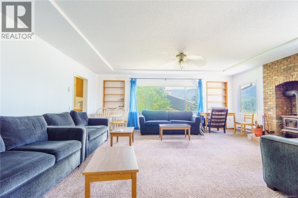 Living room with a brick fireplace, wood stove, blue sofa, armchairs, and bookshelves. - 269 Matterson Dr, Ucluelet