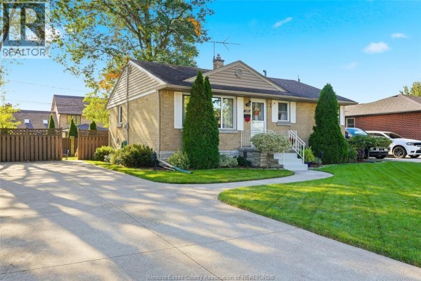 Side view of the brick bungalow showcasing the driveway and mature trees on the property. - 2691 Askin, Windsor
