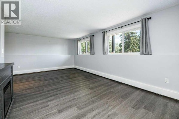Living room with grey wood-look flooring, two windows, and light grey walls. - 27, 11 Stanton Street, Red Deer