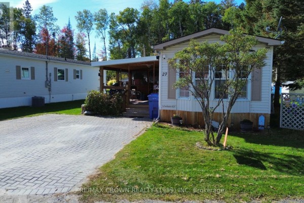 View of the mobile home from the right side, showing the lawn and a small tree. - 27 - 395 Riverbend Road, North Bay