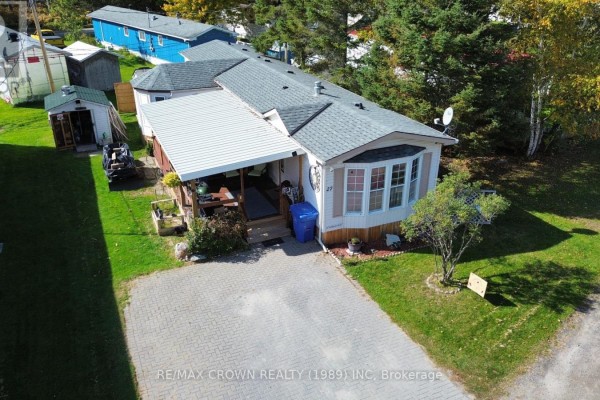 Aerial view of the mobile home with a paved driveway, covered porch, and surrounding greenery. - 27 - 395 Riverbend Road, North Bay