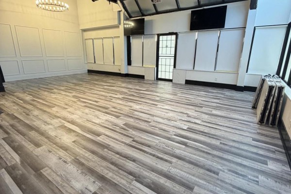 Wide view of a commercial space with wood-look flooring, white panelled walls, and stacked tables. - 27 - 501 Passmore Avenue, Toronto
