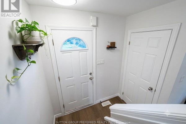 Interior entryway with white door, wood-look laminate floor, and a decorative shelf with a plant. - 27 - 825 Dundalk Drive, London South