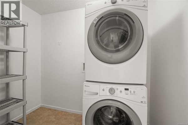 Laundry room with stacked white washer and dryer, white walls, and plastic shelving unit. - 27 2740 Stautw Rd, Central Saanich