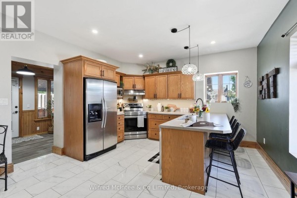Kitchen with light wood cabinets, stainless steel refrigerator, island with seating, and white tile floor. - 27 5th Street Nw, Arran Elderslie
