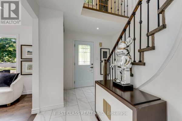 Entrance hallway with a white front door, tiled floor, and a staircase with a dark wood railing. - 27 Alton Towers Circle, Toronto