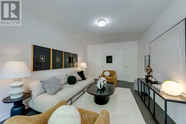 Living room with a beige sofa, two accent chairs, a dark wood coffee table, and modern artwork on the wall. - 27 Alton Towers Circle, Toronto