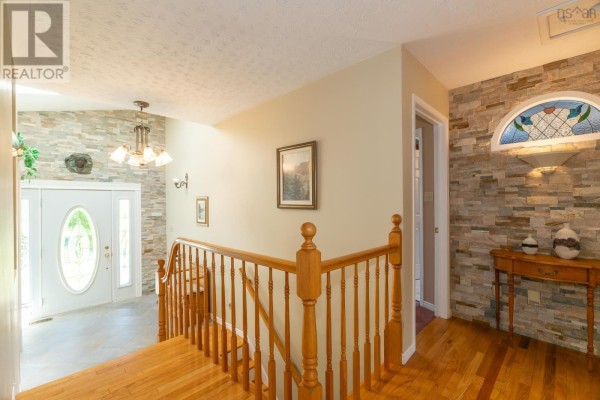 Interior view of a hallway with wood floors, a wooden banister staircase, and a stone accent wall. - 27 Basin View Lane, Upper Clements