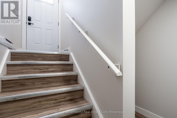 Interior staircase with wood-look laminate treads, white risers, and a white handrail on a light gray wall. - 27 Brock Street, St  Marys