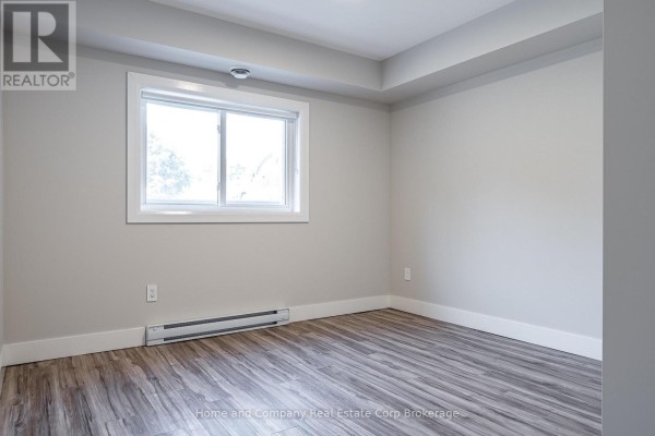 Empty room with light gray walls, wood-look laminate flooring, a single window, and a baseboard heater. - 27 Brock Street, St  Marys