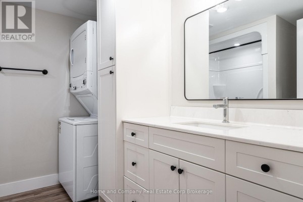 Bathroom vanity with a white countertop, white cabinets, a stainless steel faucet, and a stacked washer and dryer. - 27 Brock Street, St  Marys