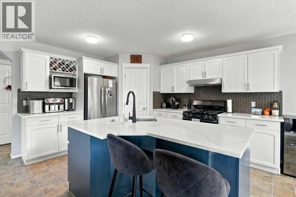 Open-concept kitchen and dining area with white cabinets, a large island, and patio doors leading to a backyard. - 27 Chapman Close Se, Calgary
