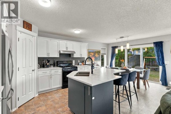 View of the kitchen island and white cabinets, with a stainless steel refrigerator and a dining area visible. - 27 Chapman Close Se, Calgary