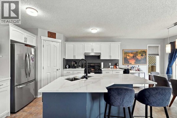 Spacious kitchen and dining area featuring white cabinetry, a large island with bar stools, and a glass-top dining table. - 27 Chapman Close Se, Calgary