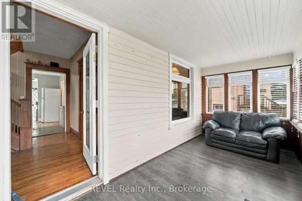 Sunroom with a black leather sofa, white paneled walls, and large windows. - 27 Christmas Street, Port Colborne