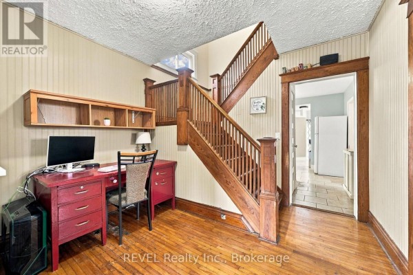 Interior view of a hallway with a wooden staircase, a red desk, and hardwood floors. - 27 Christmas Street, Port Colborne