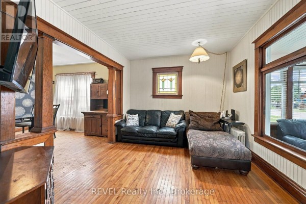 Living room with a black sofa, chaise lounge, wood floors, and large windows overlooking the street. - 27 Christmas Street, Port Colborne