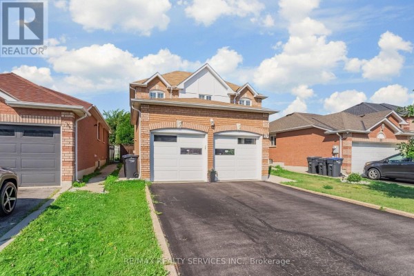 Side view of the brick house showing the double garage and driveway with green lawn. - 27 Colleyville Street, Brampton