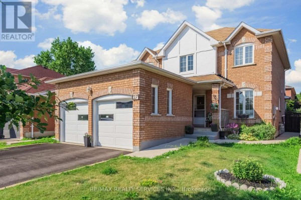 Front view of the brick house with a double garage, porch, and green lawn. - 27 Colleyville Street, Brampton