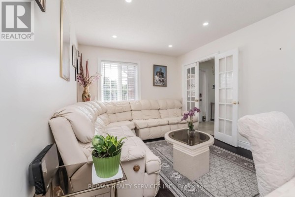 Living room with a large sectional sofa, coffee table, rug, and double glass doors. - 27 Colleyville Street, Brampton
