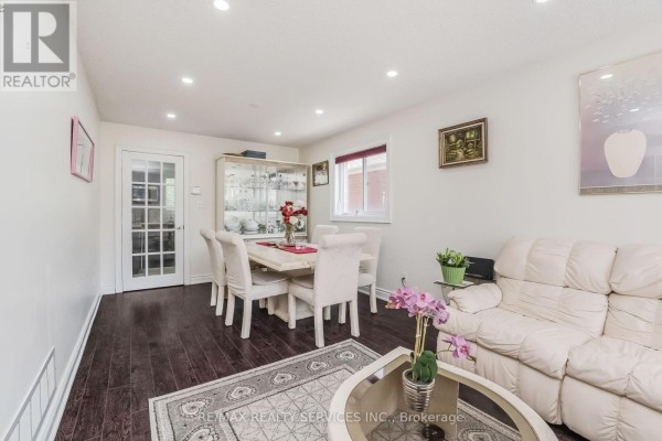 Dining room with a table and chairs, glass cabinet, sofa, and dark hardwood floors. - 27 Colleyville Street, Brampton