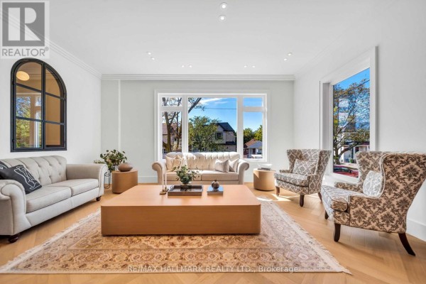 Living room with neutral sofas, patterned armchairs, a large wooden coffee table, and a patterned rug. - 27 Collinson Boulevard, Toronto