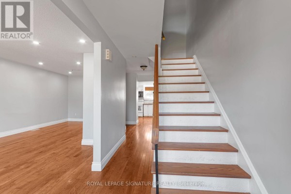 Interior view of a hallway with hardwood floors, a staircase, and doorways to living areas. - 27 Daphne Crescent, Barrie