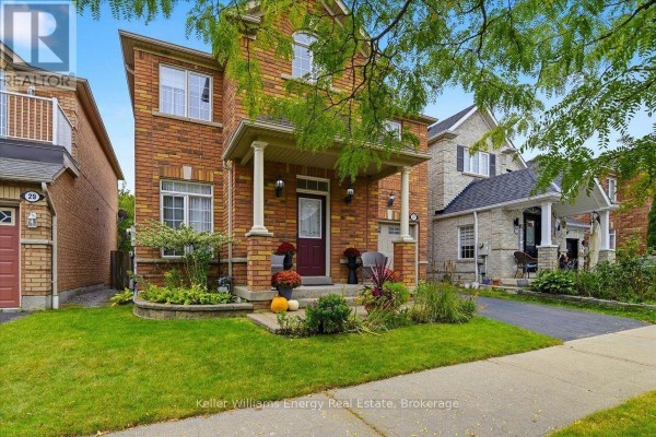 Front view of a two-story brick house with a covered porch, lawn, and surrounding landscaping. - 27 Dent Street, Ajax