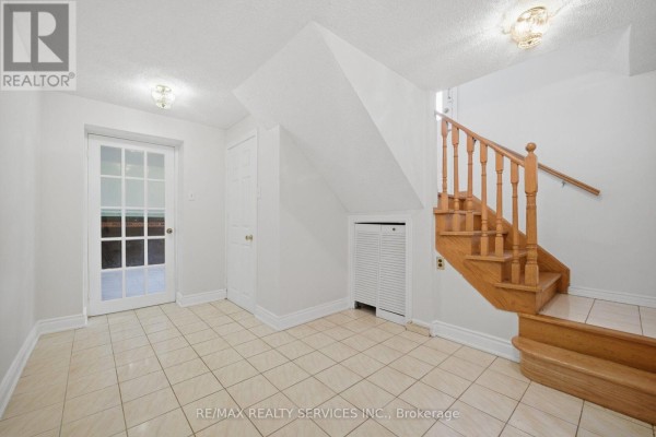 Hallway with tiled floor, wooden staircase, and glass-paneled door - 27 Edgemont Drive Brampton