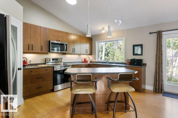 Kitchen with light wood cabinets, stainless steel appliances, island with seating, and window view. - 27 Fair Oaks Dr, St  Albert