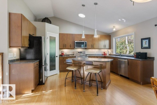 Kitchen with wood cabinetry, stainless steel appliances, island with stools, and door to backyard. - 27 Fair Oaks Dr, St  Albert