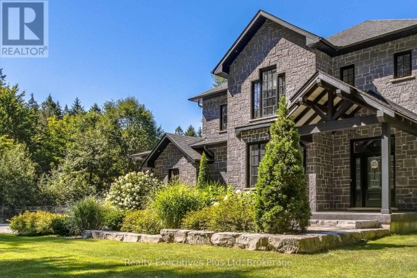 Side view of a grey stone house with large windows and landscaping. - 27 Kingfisher Crescent, Tiny