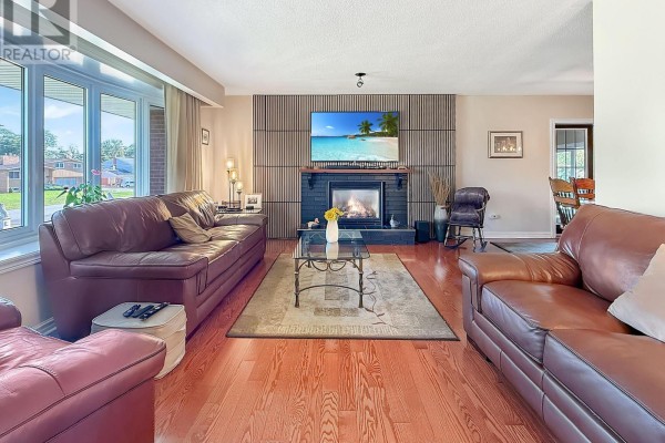 Living room with brown leather sofas, a fireplace, wood floors, and a large window. - 27 Lindbergh Drive, Fort Erie