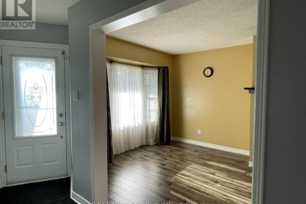 Entryway with a frosted glass door and view into a living room with wood-look flooring and yellow walls. - 27 Lindsay Court, Barrie