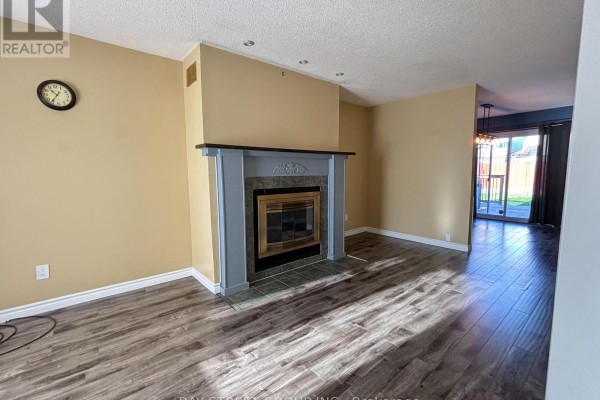 Living room with wood-look flooring, a grey fireplace, and a doorway leading to a dining area with a sliding glass door. - 27 Lindsay Court, Barrie