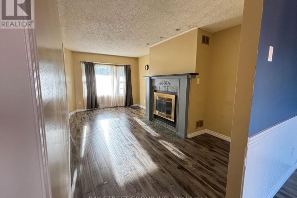 Living room with beige walls, a grey fireplace, and a view into a hallway with a dark blue accent wall. - 27 Lindsay Court, Barrie