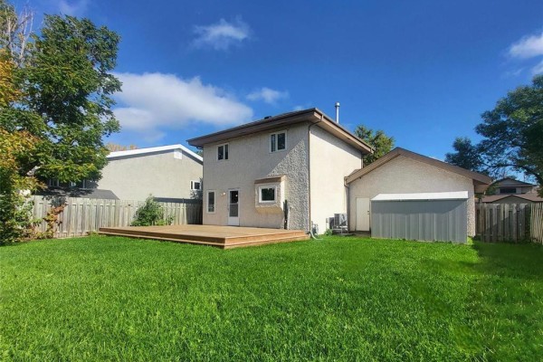 Rear exterior of a house with a wooden deck and fenced green backyard. - 27 Olford Crescent, Winnipeg
