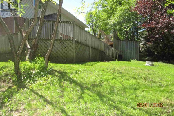 Rear view of a wooden deck and fenced backyard with green grass and mature trees. - 27 Plummer Ct, Sault Ste  Marie