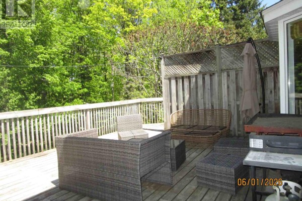 Wooden deck with wicker patio furniture, a grill, and surrounding trees. - 27 Plummer Ct, Sault Ste  Marie