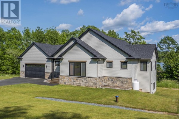 Side view of a modern white house with light grey siding, dark windows, stone foundation, and a propane tank. - 27 Prettybird Lane, Oakfield
