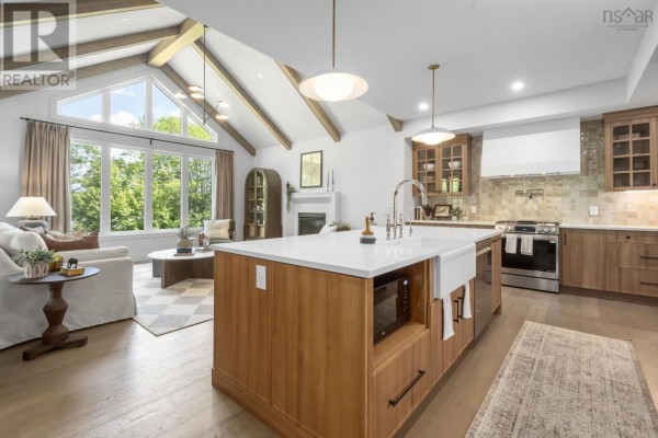 Open-concept living area with vaulted ceilings, exposed beams, a large kitchen island with a farmhouse sink, and a fireplace. - 27 Prettybird Lane, Oakfield