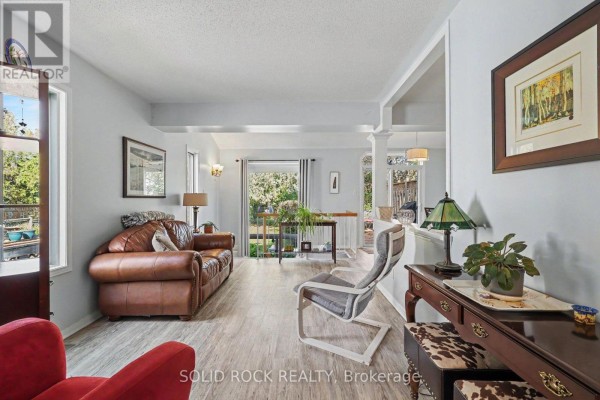 Living room with a leather sofa, chairs, a fireplace, and large windows overlooking the backyard. - 27 Randall James Drive, Ottawa
