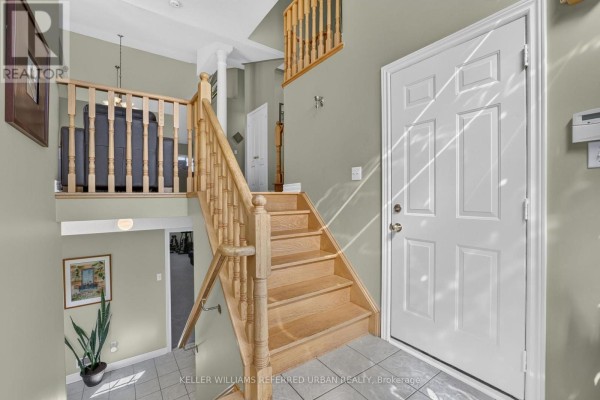Interior view showing a wooden staircase, tiled foyer, and entrance door with a hallway beyond. - 27 Summer Valley Drive, Brampton