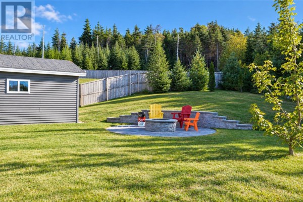 Backyard patio with stone seating wall, fire pit, and colorful chairs next to a detached garage. - 27 Summerwood Place, Portugal Cove St  Philips
