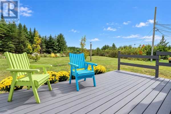 Deck with grey composite decking and brightly colored Adirondack chairs, overlooking a green lawn and trees. - 27 Summerwood Place, Portugal Cove St  Philips