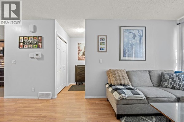 Living room with a grey sectional sofa, wood floor, and an opening to the entryway. - 27 Templemont Drive Ne, Calgary