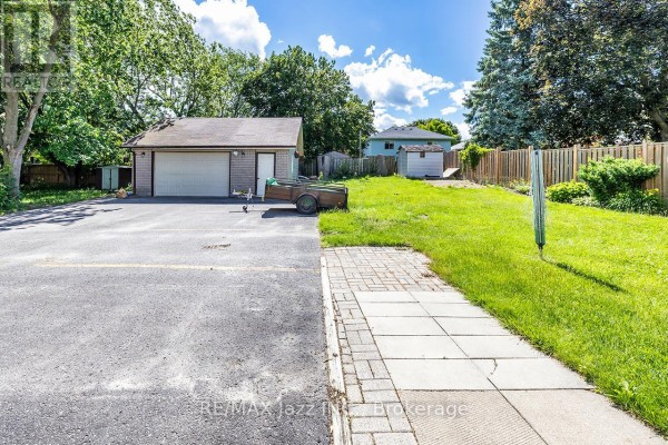 View of a detached garage, paved driveway, and backyard with a wooden fence. - 27 Waverley Road, Clarington