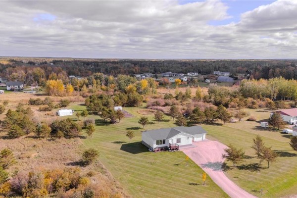 Aerial view of a white, single-story house with a gravel driveway surrounded by fields and trees. - 270 Seine River Trail, La Broquerie