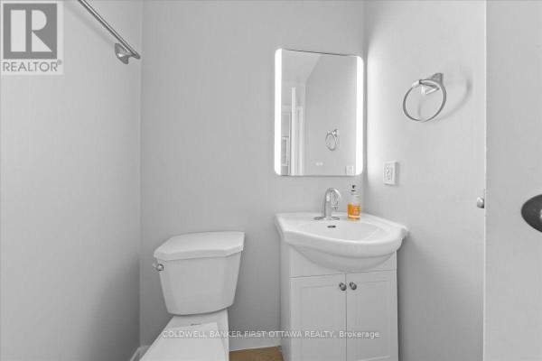 Compact bathroom with a white toilet, vanity, sink, and a modern backlit mirror. - 2701 Pimlico Crescent, Ottawa